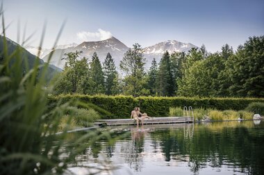 Paar am Steg des Thermalwasser Badesees mit Bergpanorama | © Alpentherme Gastein/Paul Bauer