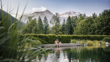 Paar am Steg des Thermalwasser Badesees mit Bergpanorama | © Alpentherme Gastein/Paul Bauer