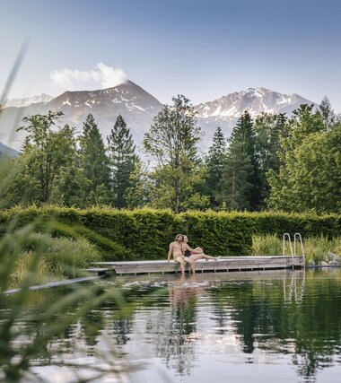 Paar am Steg des Thermalwasser Badesees mit Bergpanorama | © Alpentherme Gastein/Paul Bauer
